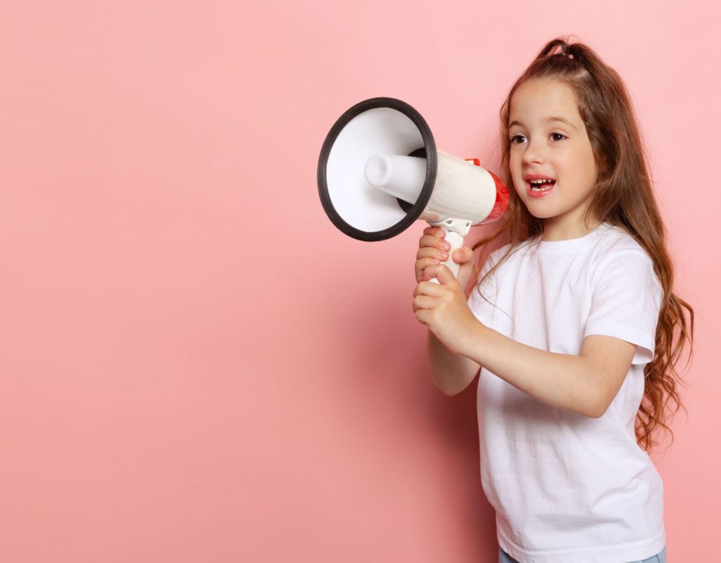 Portrait of cute little girl, child shouting in megaphone, posing isolated over pink studio background